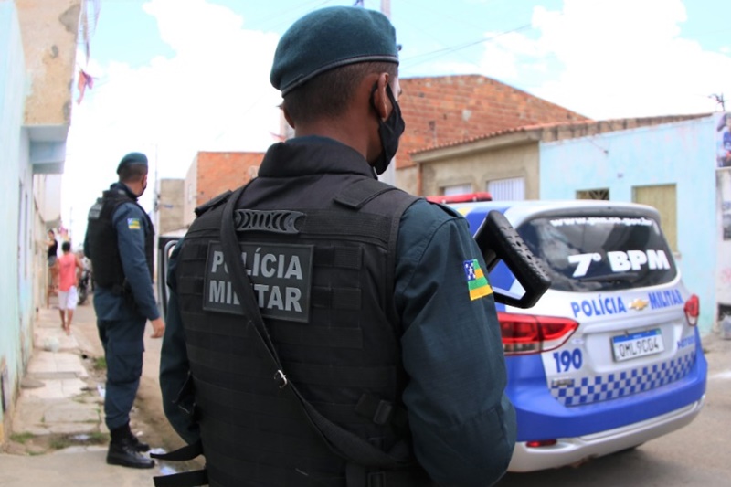 Policial Militar em pé e uma viatura
