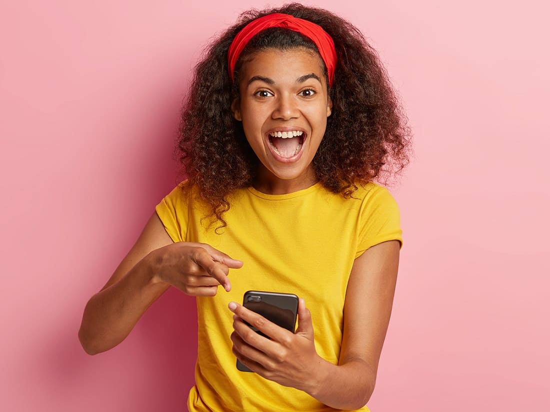 Mulher em pé apontando para o celular na mão